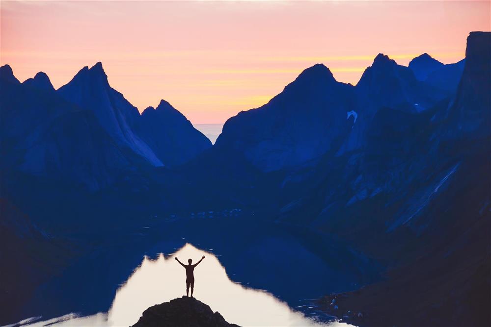 Person som står foran e fjord med mektige fjell i bakgrunnen - Klikk for stort bilde